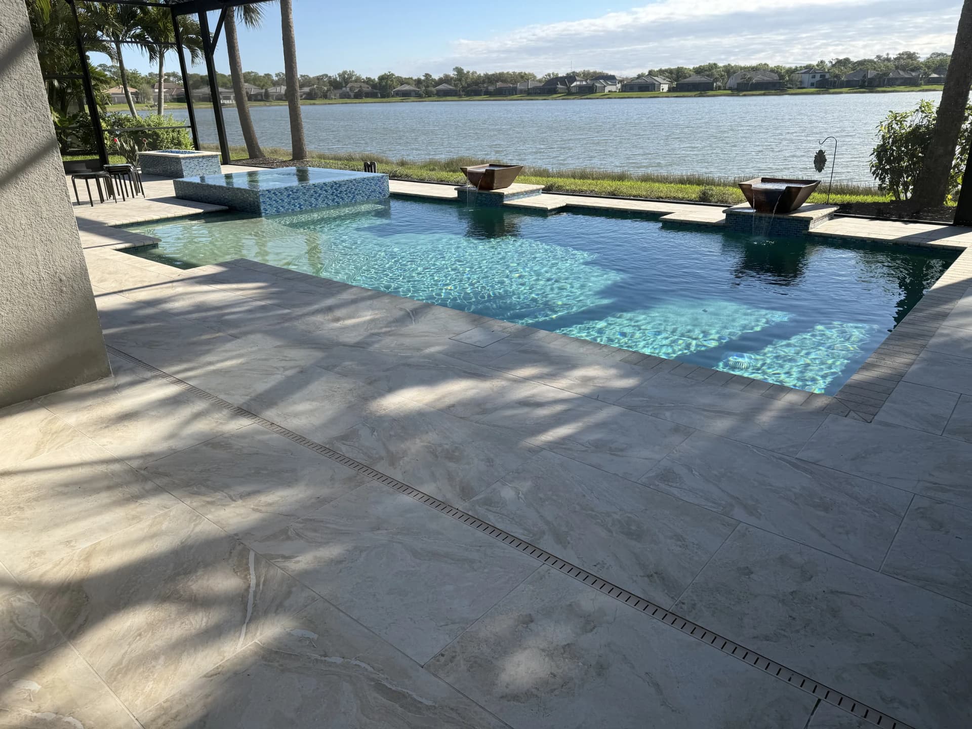 Lakefront infinity-edge pool deck with fire bowls and large-format pavers in Florida