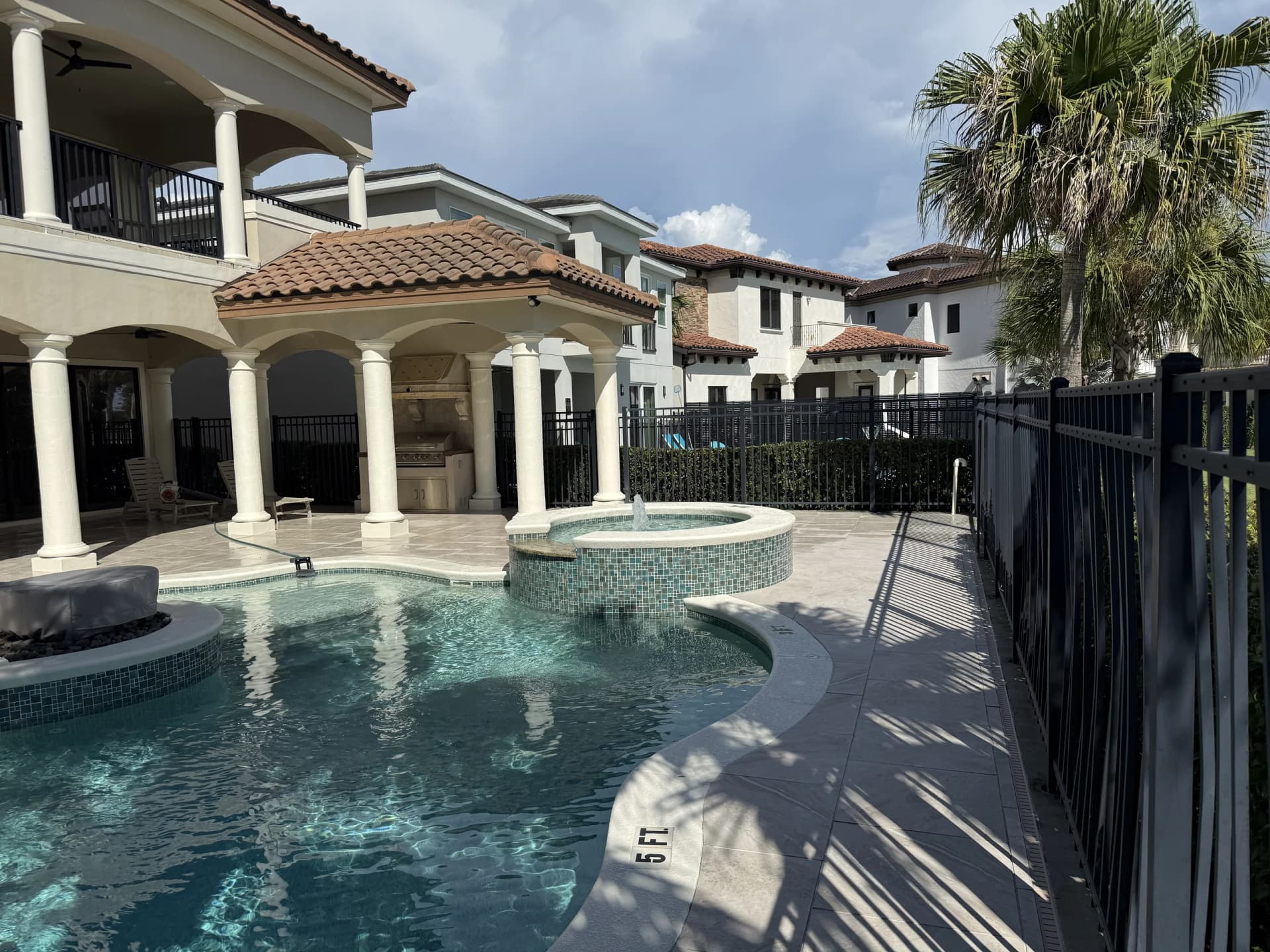 Porcelain paver pool deck and spa beside a columned luxury home in Florida