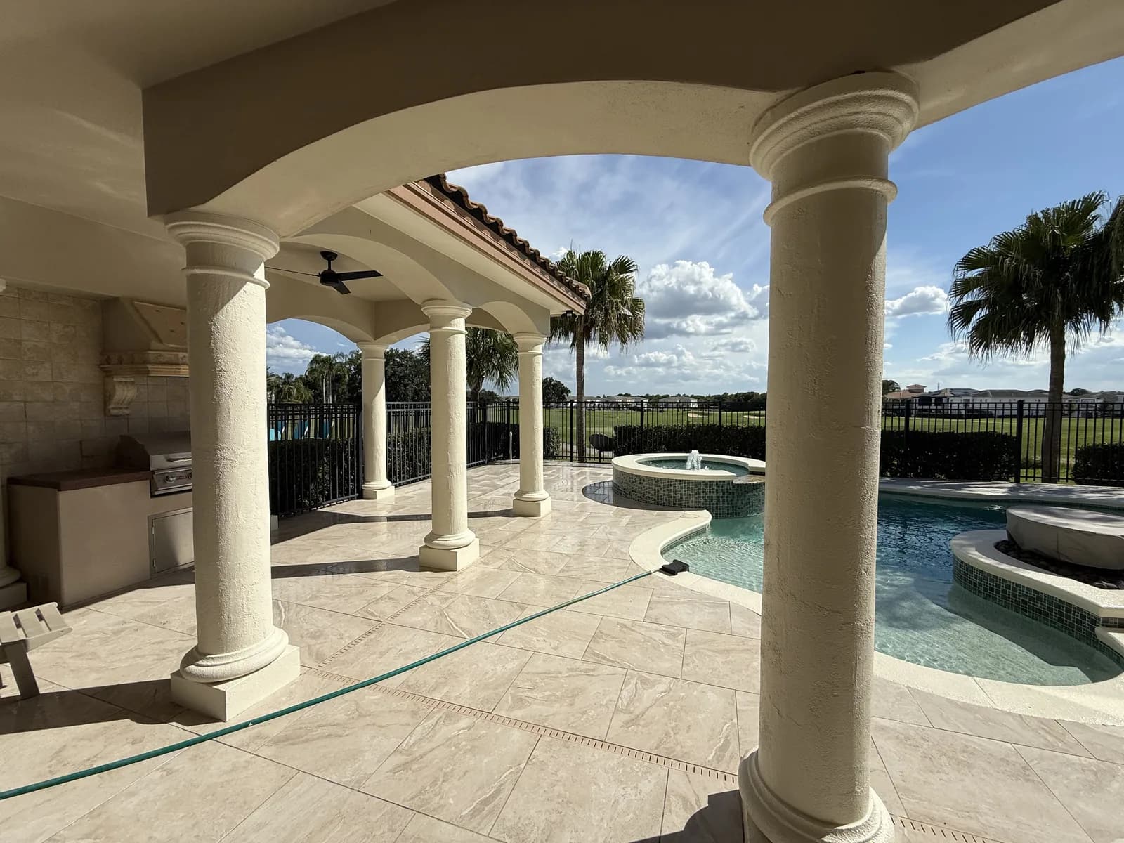 Columned lanai with paver flooring, pool and spa facing a golf course
