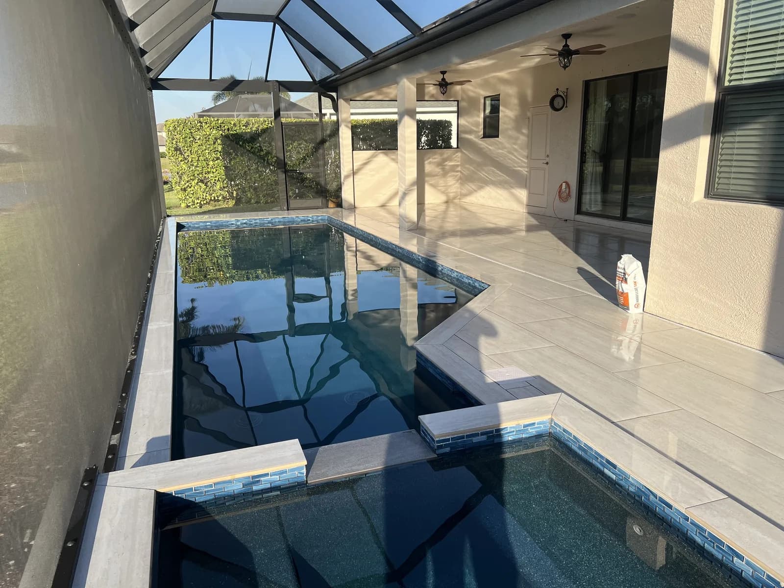 Dark infinity-edge pool with light porcelain paver deck inside a screened lanai