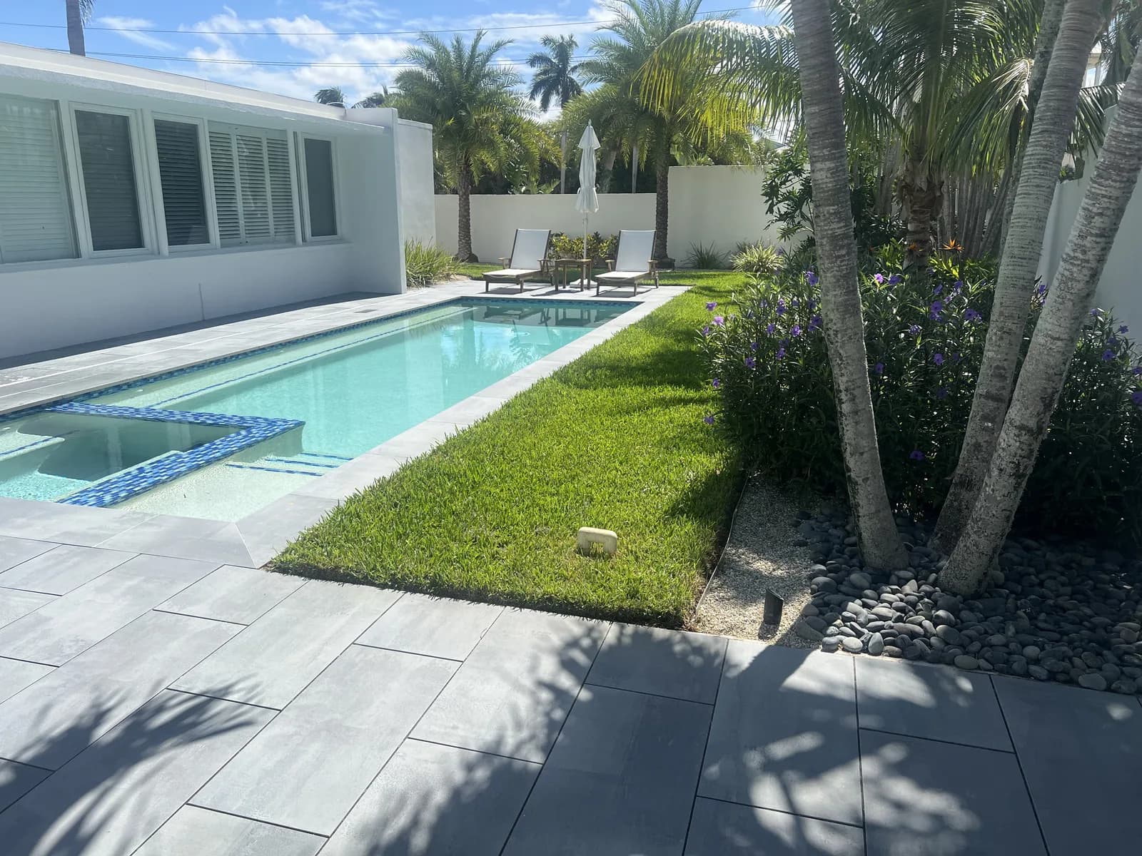 Modern lap pool with porcelain paver deck framed by palm trees
