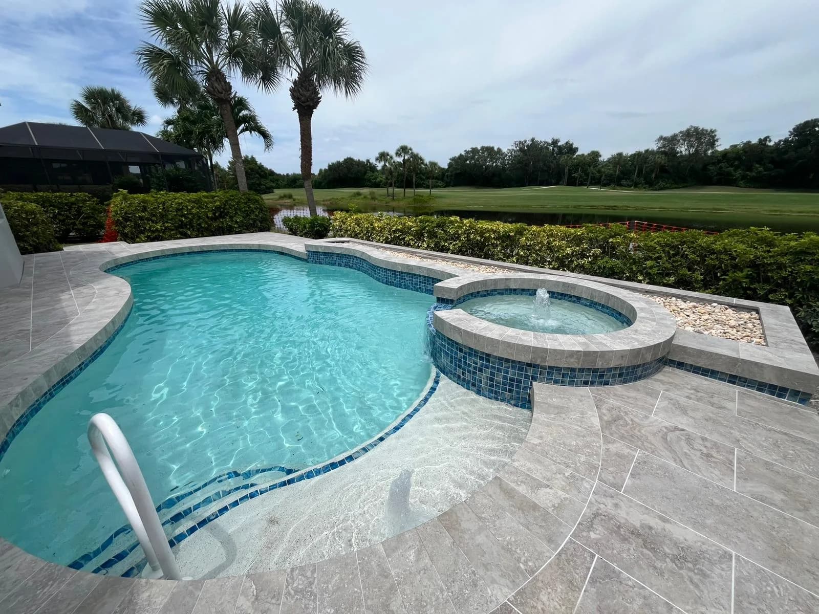 Freeform pool with attached spa and porcelain paver deck facing a golf course
