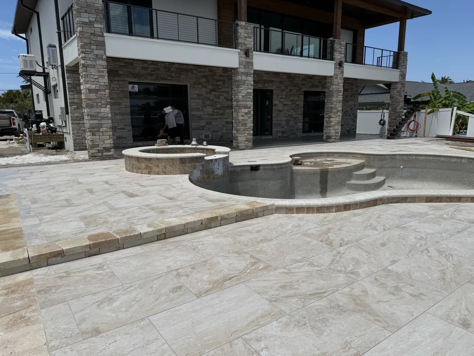 Travertine paver deck with fire pit and spa at a stacked-stone waterfront home
