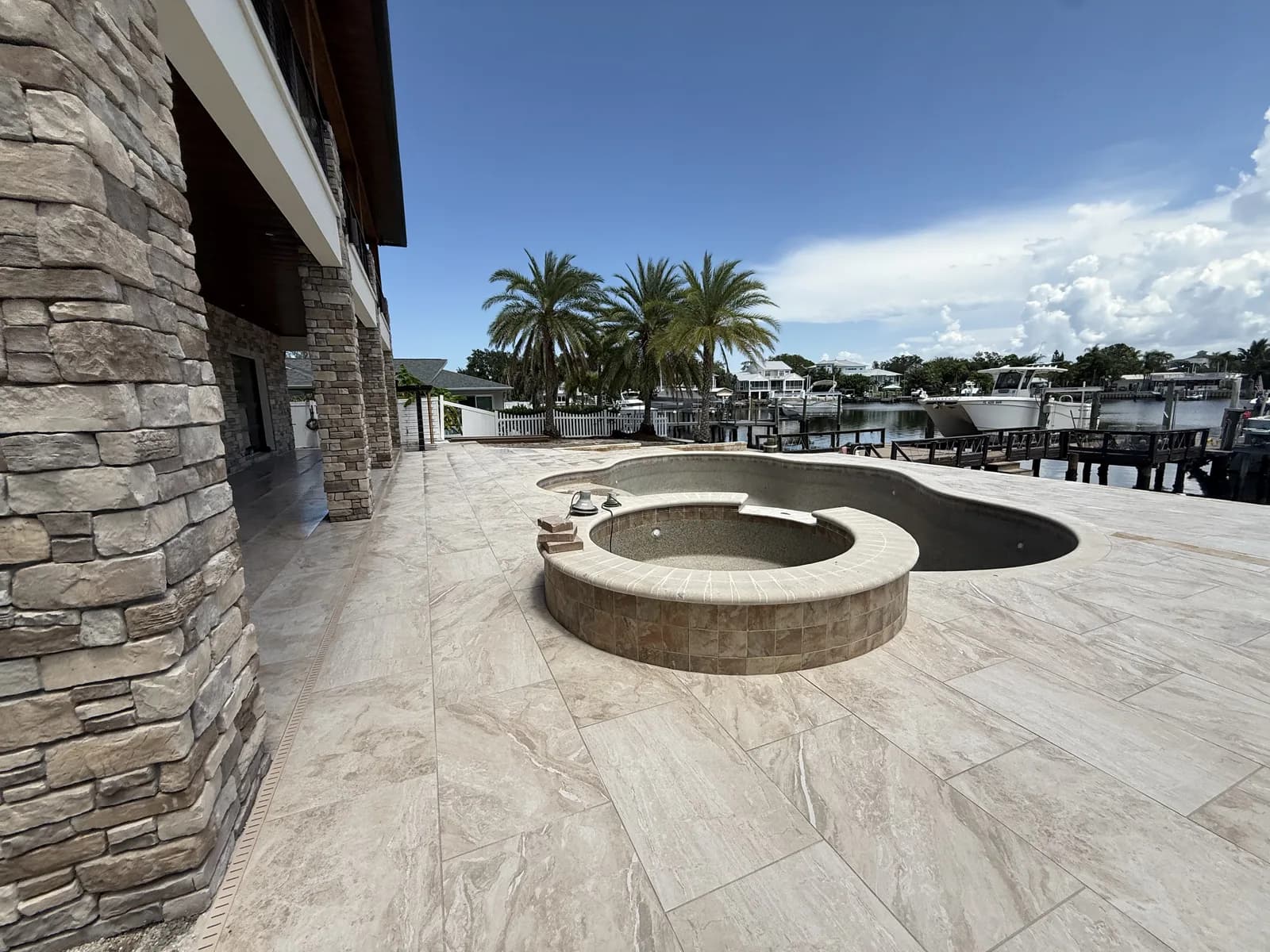 Travertine pool deck with circular fire pit beside a private boat dock