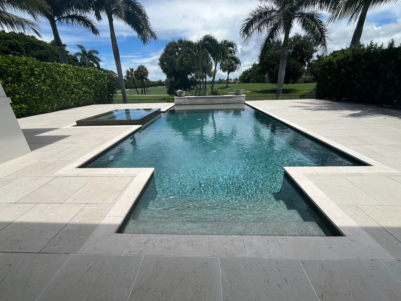 Travertine pool deck lined with palms beside a golf course fairway