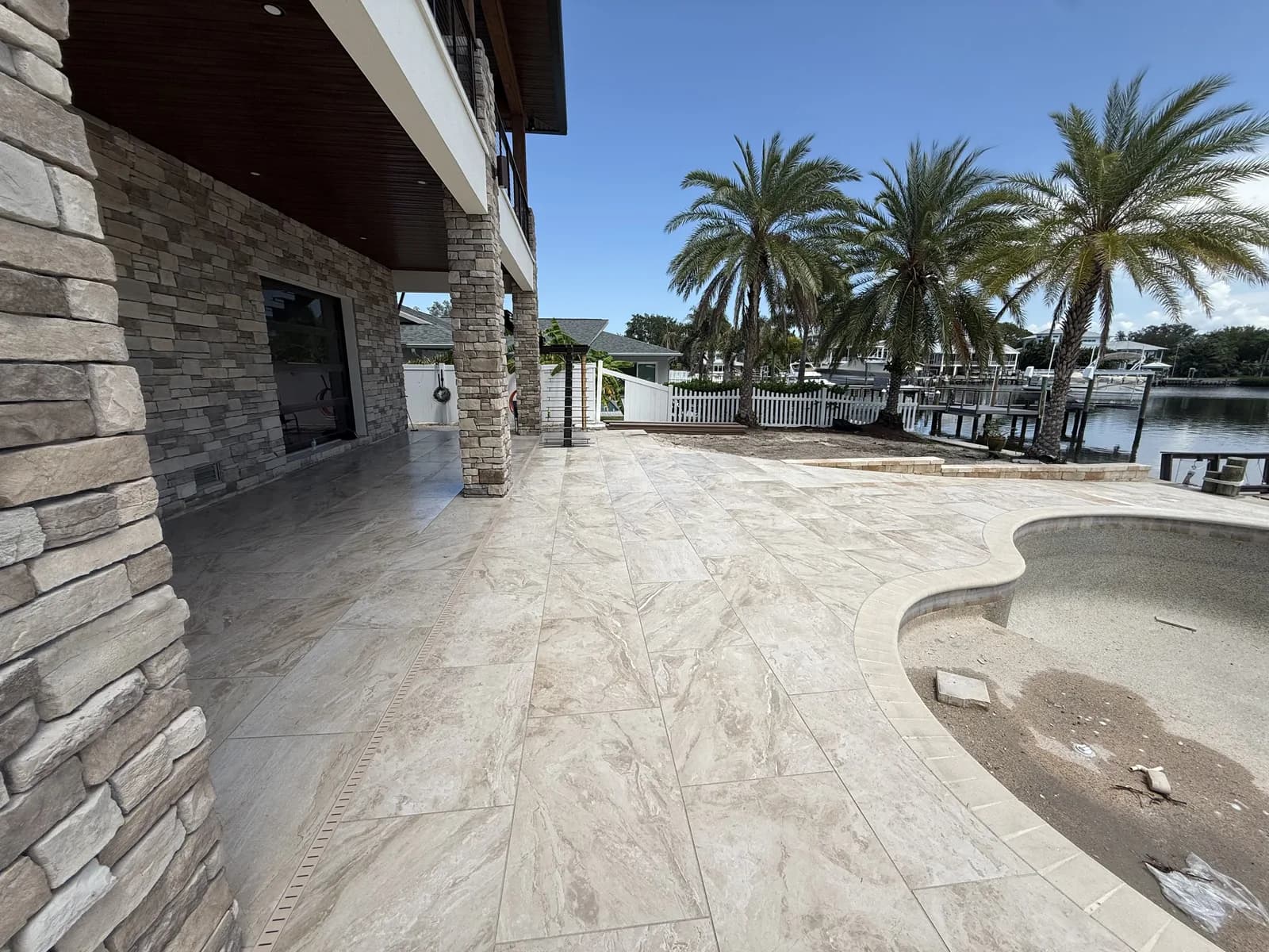 Travertine pool deck with stone accent wall and waterfront palm landscaping